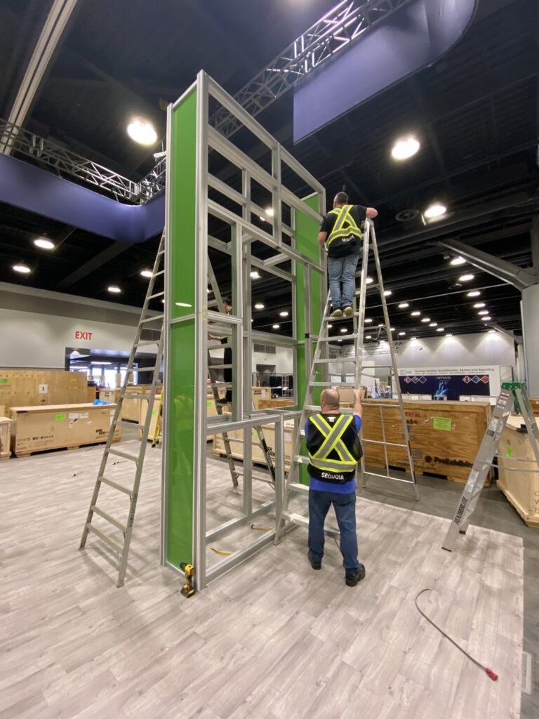 Men setting up green trade show booth on a ladder